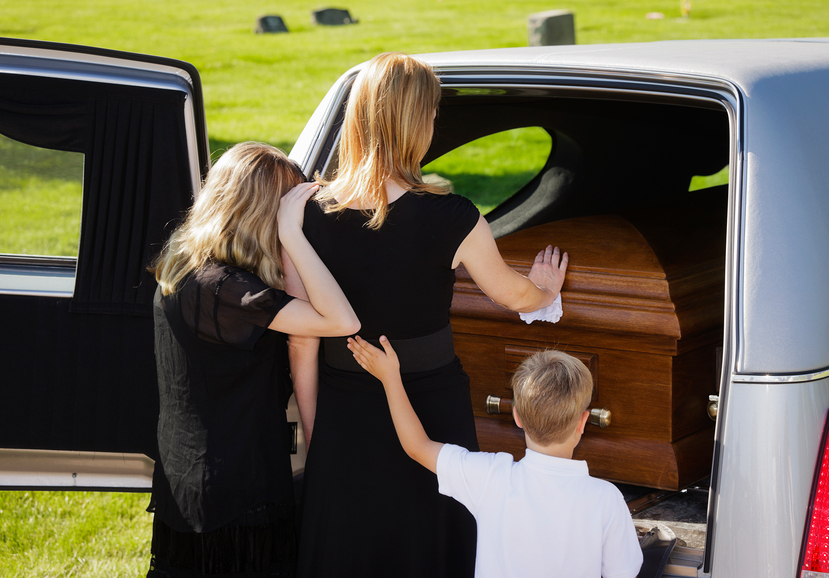 A woman and two children standing behind an open hearse.