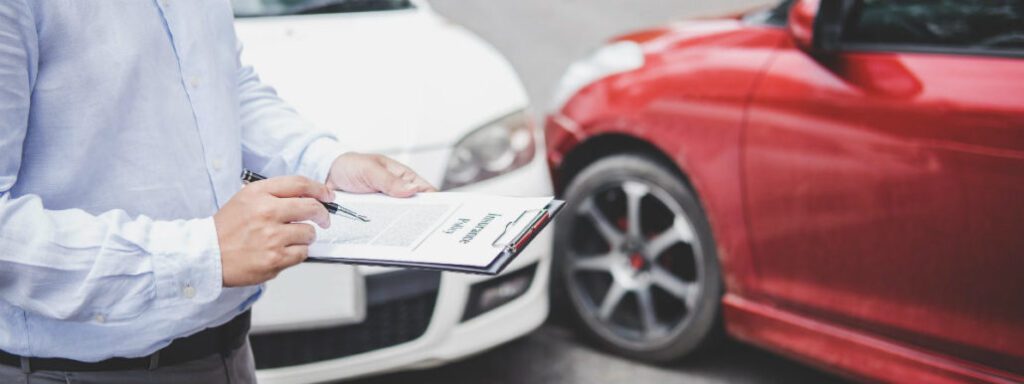 a photo a man standing beside a two cars that collide while holding a pen and writing in a paper