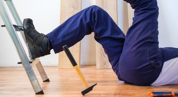 A photo of a man falling on the floor beside a metal ladder and a falling hammer.